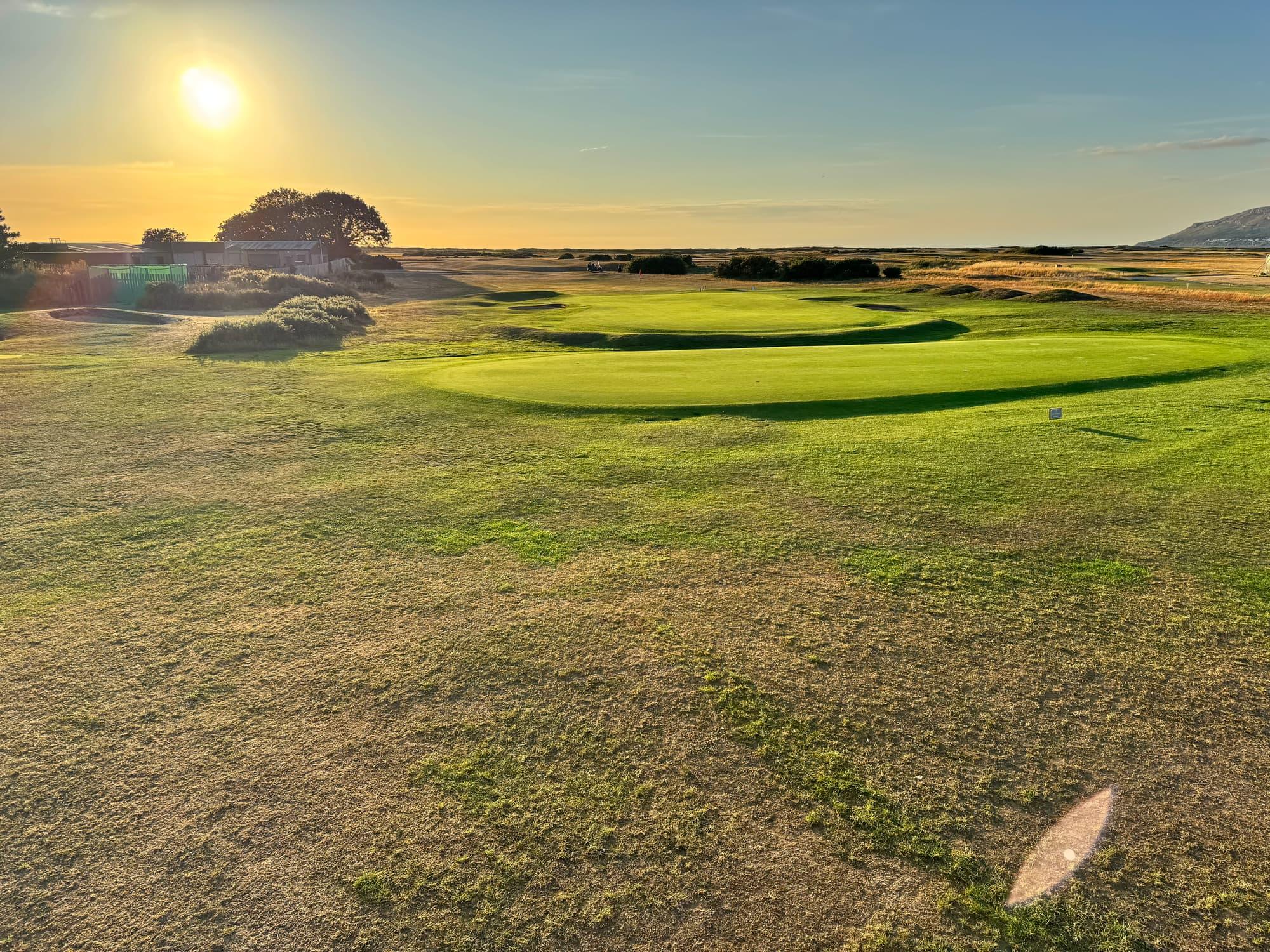An empty links green and its surrounds under a low sun, the last of the light across the turf